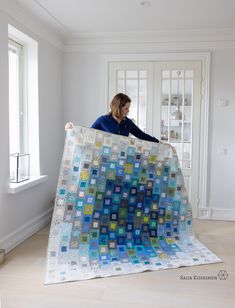 a woman is holding up a quilt in the middle of a room with white walls