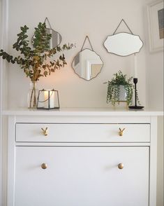 a white dresser with three mirrors above it and a potted plant on the top