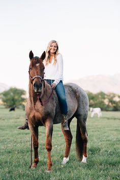 a woman riding on the back of a brown horse in a green grass covered field