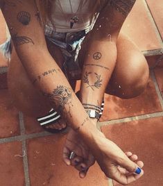 a woman sitting on the ground with tattoos on her arms and legs, both holding hands together