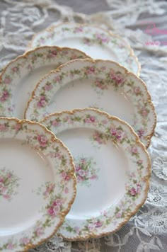 four plates with pink flowers on them are sitting on a lace tablecloth next to a white doily