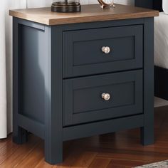 a night stand with two drawers and a clock on the top, next to a bed