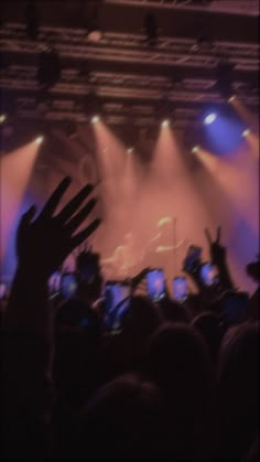 the crowd is at a concert with their hands in the air and lights coming from behind them