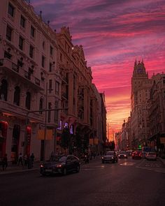 cars are driving down the street in front of tall buildings at sunset or sunrise time