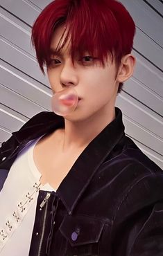 a young man with red hair blowing out his bubble while wearing a black jacket and white t - shirt