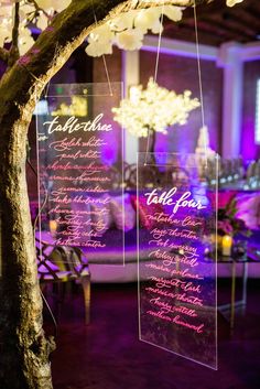 the reception table is set up with purple lighting and menus hanging from trees in front of them