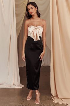 a woman standing in front of curtains wearing a black and white dress with a bow at the waist