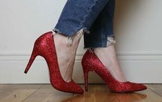 a woman wearing red glitter high heels standing on top of a hard wood floor next to a wall