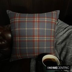 a cup of coffee sitting next to a plaid pillow