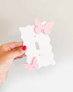 a hand holding a light switch plate with pink butterflies on it and a white background