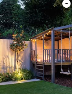 a backyard area with a swing set and lights on the deck, next to a white fence