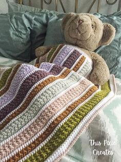 a teddy bear laying on top of a crocheted blanket next to a pillow