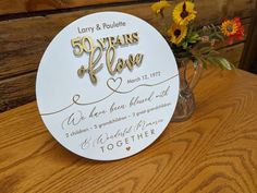 a 50th wedding anniversary plaque on a wooden table with flowers in the vase behind it