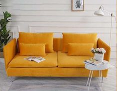 a yellow couch sitting in front of a white wall next to a potted plant