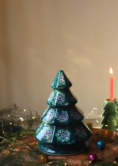 a small ceramic christmas tree sitting on top of a table next to a lit candle