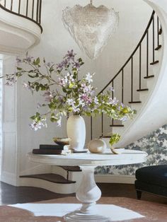 a vase with flowers sitting on top of a table in front of a spiral staircase