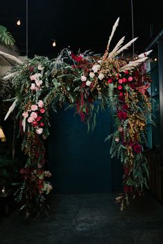 an arch made out of flowers and greenery hangs from the ceiling in front of a blue wall