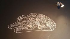 a drawing of a star wars millennium falcon on a black surface next to a light bulb