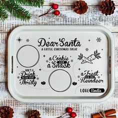 a white tray with christmas sayings on it and pine cones next to the tray