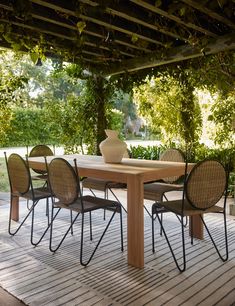 a table and chairs on a deck under a pergolated roof with trees in the background