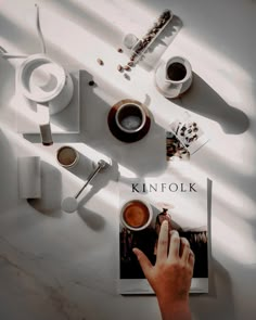 a person's hand on top of a book next to coffee cups and spoons