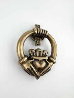 a gold colored brooch with two hands holding a heart and crown on it's side