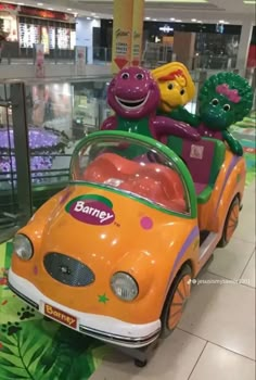 an orange toy car with peppa pig on top in a shopping mall aisle next to other toys