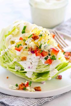 a white plate topped with lettuce covered in cheese and toppings next to a bowl of ranch dressing