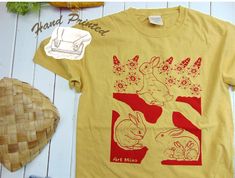 "= Rabbit Hole = They have a playroom, a powder room, and a nursery Rabbit Hole \" 100% American Grow Cotton Unisex T-shirt. This soft garment-dyed bunny tee, illustrated and hand-printed with Silk Screen by Mina Wilcox, was created with pure joy from her small art studio in California. We only use non-toxic water-based inks, ensuring they are safe for you and the Earth. Made from 100% ring-spun cotton, responsibly sourced from American farms, and carefully garment-dyed, this tee exudes a retro look and feel. DETAILS: One 100% American Grow Cotton Garment Dyed Short Sleeve T-shir *Garment dyeing offers a remarkable method for creating trendy and captivating apparel with a beloved, well-worn t-shirt appearance. This aesthetic is achieved by applying the dye to the clothing after it has unde Grow Cotton, Small Art Studio, Relax Lifestyle, Bunny T Shirt, Toxic Water, Tshirt Art, The Dye, Hand Screen Printed, Pure Joy