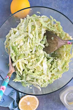 a glass bowl filled with coleslaw next to an orange and a wooden spoon