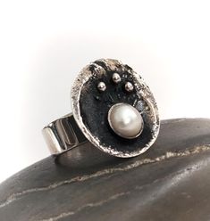 The most stunning and quite unique Silver and Pearl Danish Swedish / modernist / brutalist styled ring. The ring is hallmarked 925 and depicts a bowl or cauldron containing a pearl and smaller silver balls. Very unusual and quite striking and in perfect condition.  The ring is an English size P and a 7.5 US. The pen is just for scale and not included. Please feel free to ask any questions, I'm happy to help, and many thanks for visiting our new Etsy store. Brutalist Ring With Oxidized Finish As Gift, Hand Forged Sterling Silver Modernist Rings, Brutalist Oxidized Finish Ring For Gift, Modern Oxidized Finish Rings For Anniversary, Brutalist Oxidized Finish Ring As Gift, Modernist Hand Forged Sterling Silver Rings, Modern Oxidized Finish Anniversary Ring, Oxidized Finish Oval Rings For Anniversary, Oval Rings With Oxidized Finish For Anniversary