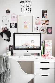 a computer monitor sitting on top of a desk next to a white chair and wall covered with pictures