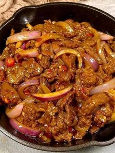 a skillet filled with meat and onions on top of a table