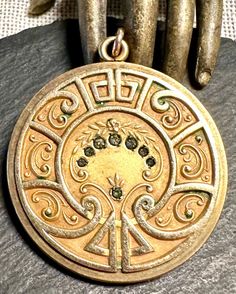 a gold colored pendant with an intricate design on it's face and two hands behind it