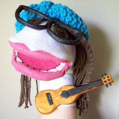 a doll with glasses and a guitar on her arm, wearing a knitted hat