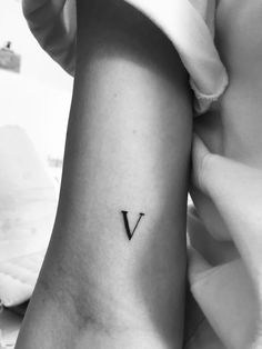 a black and white photo of a woman's arm with a small v tattoo on it