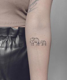 an elephant tattoo on the left arm is shown in black and grey ink, with three smaller elephants behind it