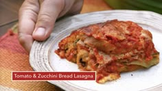 a white plate topped with lasagna covered in cheese and tomato sauce next to a persons hand