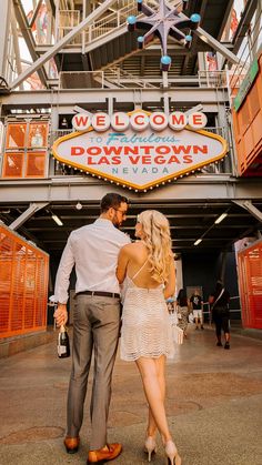 a man and woman standing in front of the welcome to downtown las vegas sign