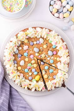 a large cake with white frosting and colorful candies on the top is cut into pieces