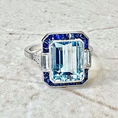 Did you know Aquamarine, the birthstone for March was the blue variety of the Beryl family which also includes Emerald, Morganite, Goshenite, Yellow & Red Beryl? 💙 #BlueLove #HappyBirthday This Art Deco style ring centers a fine emerald cut aquamarine weighing 3.23 carats. It is haloed by a row of French cut sapphires, and a pair of matching baguette diamonds. It is shouldered by six old European cut diamonds. #Rings #FineJewelry #VintageStyle #ArtDecoStyle #ArtDeco #AquamarineRing #Luxury Art Deco Sapphire Ring, Aquamarine Engagement Ring, French Cut, Diamond Halo Ring, Aquamarine Jewelry, Baguette Diamonds, Aquamarine Rings, European Cut Diamonds, Halo Diamond Ring