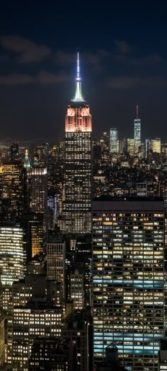 the empire building is lit up at night in new york city, with other skyscrapers visible