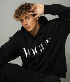 a young man with curly hair wearing a black hoodie and sitting on the floor