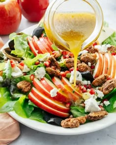 an apple salad with dressing being poured into it on a white plate next to apples