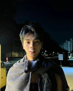 a young man standing in front of a parking meter at night with his scarf around his neck