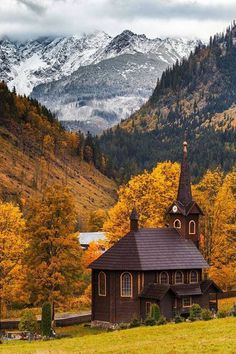 an old church in the mountains surrounded by trees with yellow leaves on it's roof