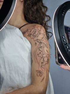 a woman with a flower tattoo on her arm holding a cell phone up to the camera