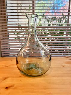 a glass vase sitting on top of a wooden table next to a window with blinds