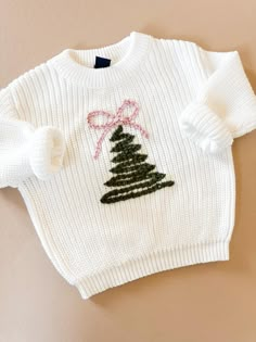 a white sweater with a pink bow on the front and green tree on the back