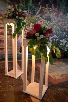 two white vases with flowers and greenery on them